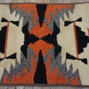 Highly textured rug with a geometric pattern in cream, black, orange, and grey on rustic wood flooring.
