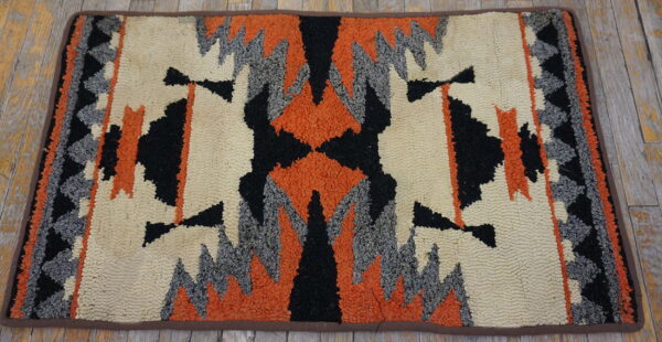 Highly textured rug with a geometric pattern in cream, black, orange, and grey on rustic wood flooring.