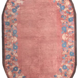 A pink oval rug featuring a detailed floral and trellis border in blue, cream, and brown.