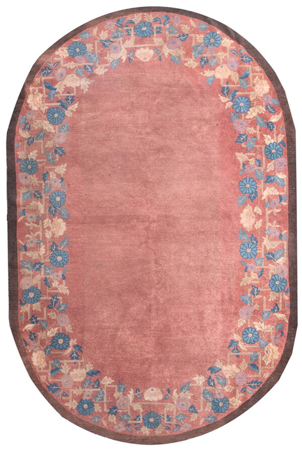 A pink oval rug featuring a detailed floral and trellis border in blue, cream, and brown.