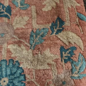 Detail shot of a dense, textured pile rug featuring rose, teal, and beige traditional floral designs.