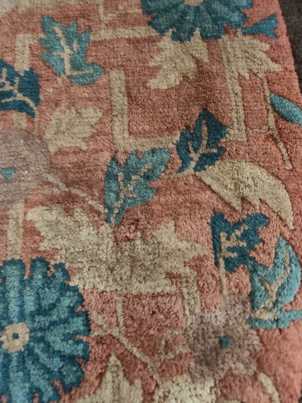 Detail shot of a dense, textured pile rug featuring rose, teal, and beige traditional floral designs.
