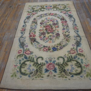 A cream rug with an oval multicolored floral pattern rests on distressed wooden floorboards.