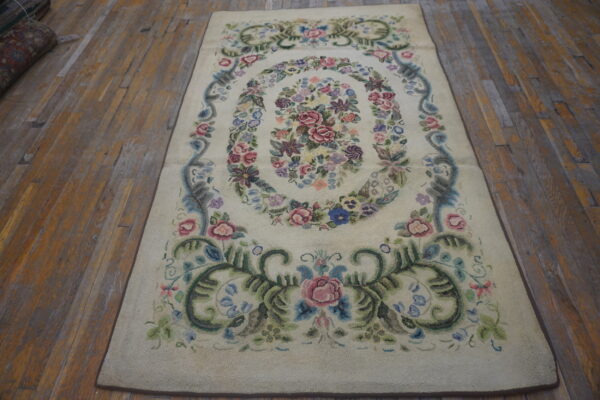 A cream rug with an oval multicolored floral pattern rests on distressed wooden floorboards.