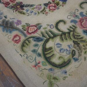 Cream textured rug displaying pink, blue, and green floral scrollwork next to dark distressed wood flooring.
