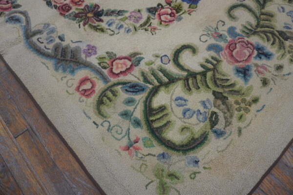 Cream textured rug displaying pink, blue, and green floral scrollwork next to dark distressed wood flooring.