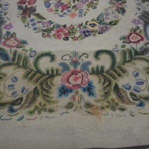 Cream hooked rug detail showing pink roses, green leaves, and blue scrolls in a dense floral pattern.