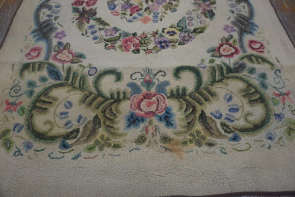 Cream hooked rug detail showing pink roses, green leaves, and blue scrolls in a dense floral pattern.