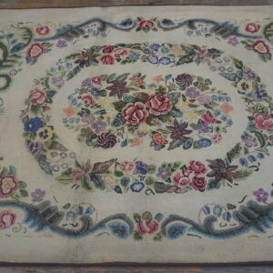 Cream textured rug with a detailed multicolored floral medallion and scrolling border on wooden floorboards.