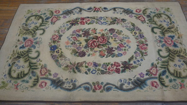 Cream textured rug with a detailed multicolored floral medallion and scrolling border on wooden floorboards.