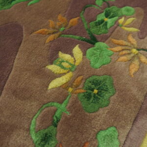 Sculpted pile rug detail shows green, yellow, and orange flowers on a brown field next to lime green fringe.