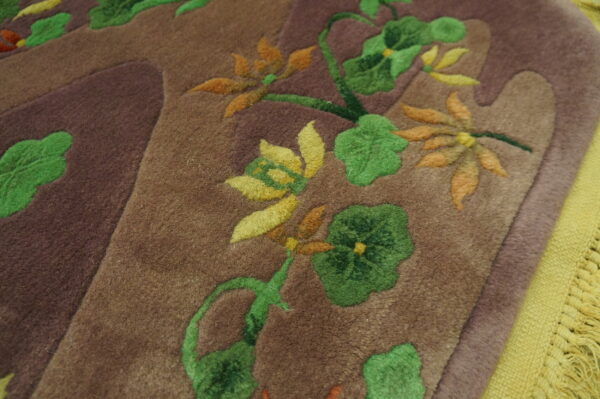 Sculpted pile rug detail shows green, yellow, and orange flowers on a brown field next to lime green fringe.