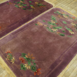 Two mauve rugs with carved orange and green floral designs and light fringe rest on plank wood floors.