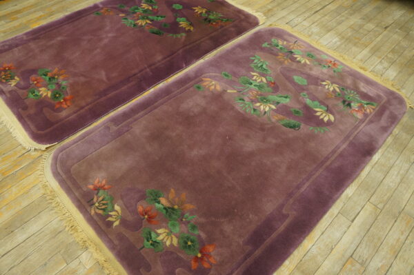 Two mauve rugs with carved orange and green floral designs and light fringe rest on plank wood floors.