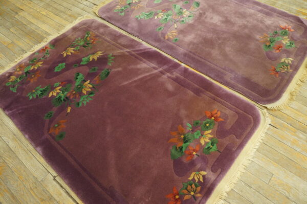Two plum rugs with carved orange and green floral motifs lay on light wooden plank flooring.
