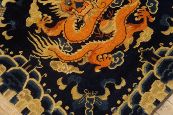 Dark navy rug detail showing an orange and gold dragon design with blue accents on wood flooring.