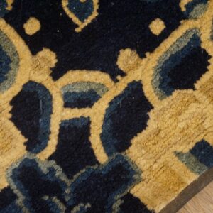 Textured navy rug with a bold, stylized gold and blue pattern rests on light wood planks.