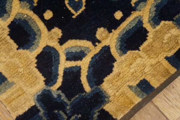 Textured navy rug with a bold, stylized gold and blue pattern rests on light wood planks.