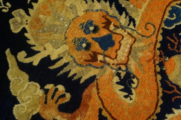 Close-up detail of a textured rug showing an orange and yellow dragon motif on a dark navy background.