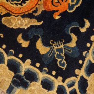 Close-up of a textured high-pile rug in gold, orange, and blue with ornate stylized motifs.