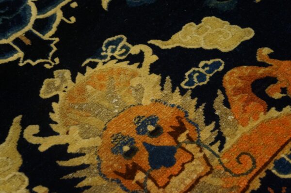Close-up shows a navy blue rug pattern featuring orange and yellow figures surrounded by stylized blue and gold clouds.