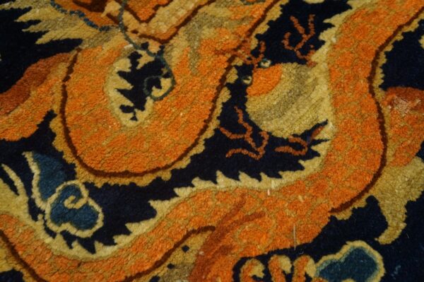 Textured rug pile displays a bold, scrolling pattern in high-contrast orange, navy blue, and gold colors.