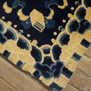 Close-up of a plush navy and beige patterned rug lying on distressed, light brown wooden floorboards.