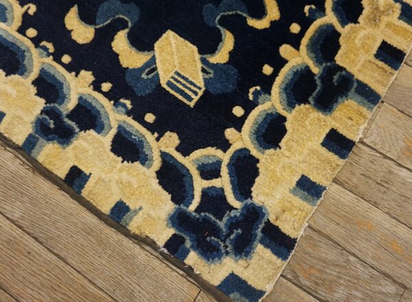 Close-up of a plush navy and beige patterned rug lying on distressed, light brown wooden floorboards.
