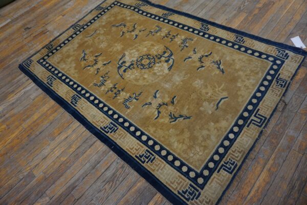 Gold rug with a central medallion, blue borders, and floral motifs rests on distressed wood plank flooring.