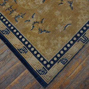 Low-pile rug in gold and navy blue with floral designs and complex borders on weathered wood flooring.