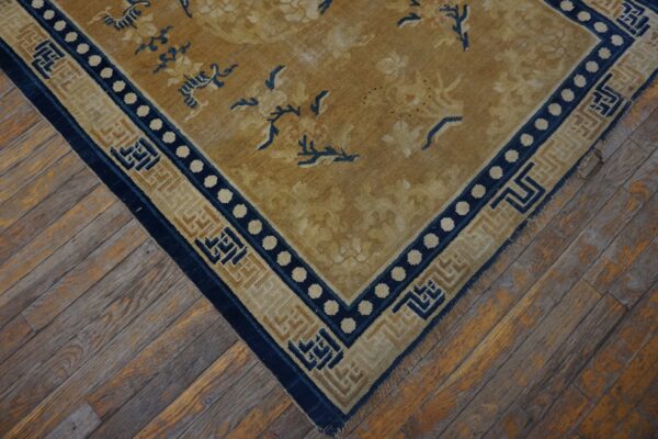Low-pile rug in gold and navy blue with floral designs and complex borders on weathered wood flooring.