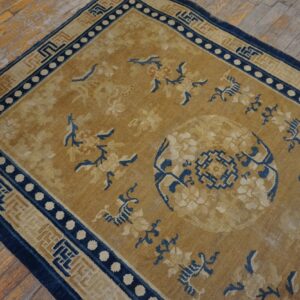 Tan and navy patterned rug with a floral medallion, bordered by geometric designs on distressed wood flooring.