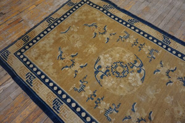 Tan and navy patterned rug with a floral medallion, bordered by geometric designs on distressed wood flooring.