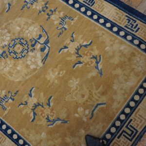 Ocher rug with blue floral and geometric patterns, featuring a dotted border, lies on wood planks.