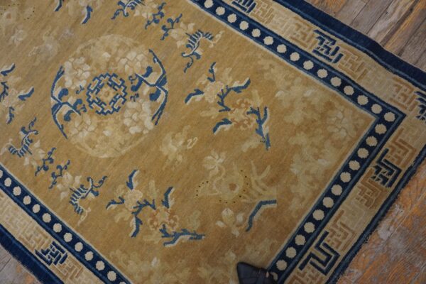 Ocher rug with blue floral and geometric patterns, featuring a dotted border, lies on wood planks.