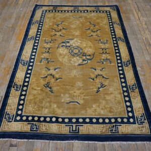 Gold and navy patterned rug with a central medallion lies on worn light wood flooring.