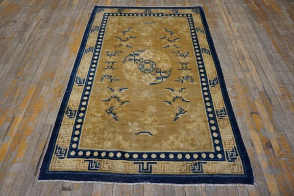 Gold and navy patterned rug with a central medallion lies on worn light wood flooring.