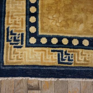 Gold rug corner with navy key and polka dot borders rests upon weathered wooden planks.