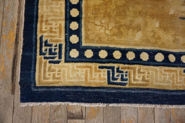 Gold rug corner with navy key and polka dot borders rests upon weathered wooden planks.
