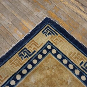 Navy and beige geometric border rug corner shows white dots on distressed gray wood floor.