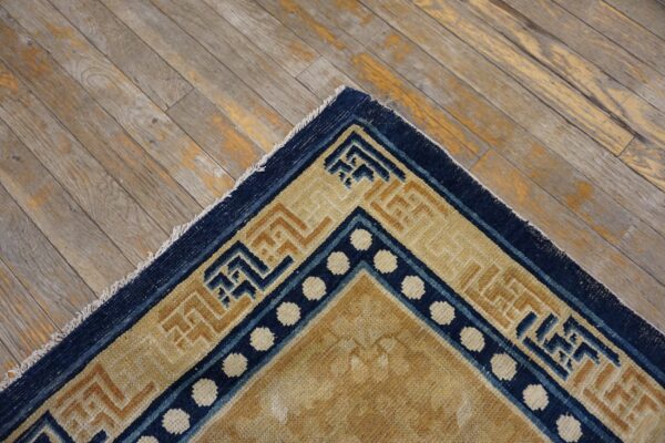 Navy and beige geometric border rug corner shows white dots on distressed gray wood floor.