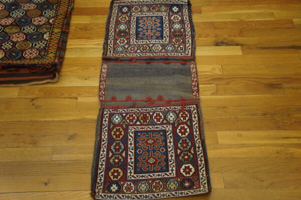 A double-panel geometric woven textile in red, blue, and gray, displayed flat on a golden wood plank floor.
