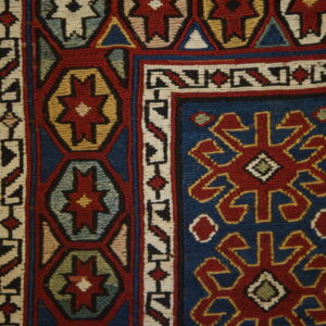 Detail of a tight flatweave rug featuring blue, red, cream, and gold tribal geometric patterns on hardwood.