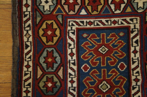 Detail of a tight flatweave rug featuring blue, red, cream, and gold tribal geometric patterns on hardwood.