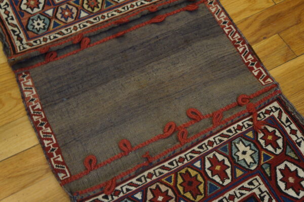 Geometric patterned flatweave textile folded over a plain gray panel accented with decorative red braided trim.