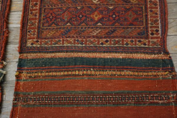 Woven textile with a geometric red and blue border above wide flatweave stripes on weathered wood.