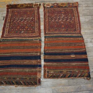 Two reddish, geometric textiles with striped flat-woven ends laid parallel on distressed gray wood flooring.
