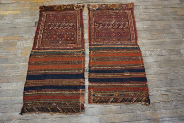 Two reddish, geometric textiles with striped flat-woven ends laid parallel on distressed gray wood flooring.