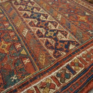 A highly textured geometric rug featuring rust, navy, and teal patterns rests on weathered gray wood.
