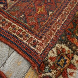 Rust-colored geometric rug detail showing flatweave and shaggy textures, resting on distressed gray wood planks.